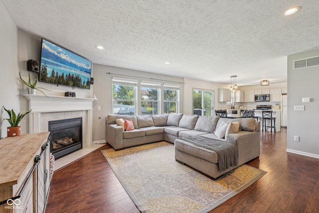living room with a tiled fireplace, recessed lighting, a textured ceiling, and dark wood-type flooring
