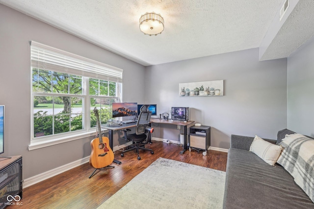 office area with baseboards, a textured ceiling, wood finished floors, and visible vents
