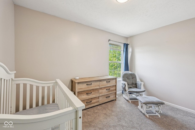 bedroom with baseboards, carpet flooring, a crib, and a textured ceiling