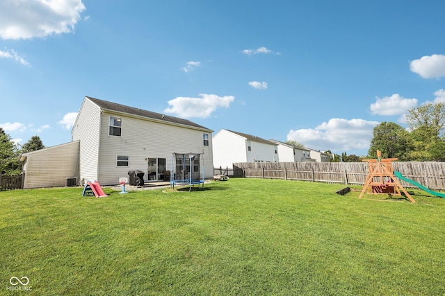 rear view of property featuring a playground, a trampoline, a lawn, and a fenced backyard