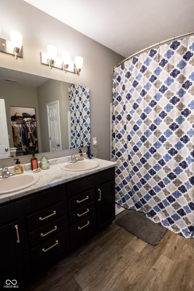 bathroom featuring double vanity, curtained shower, a sink, and wood finished floors