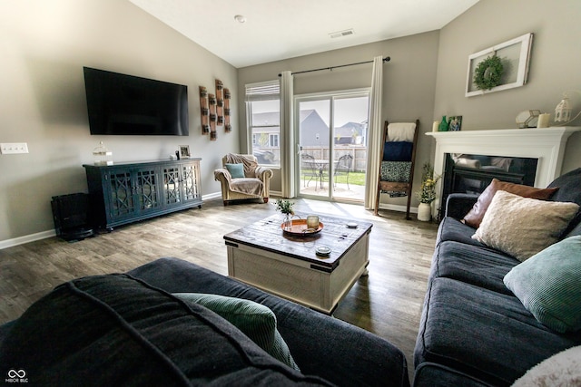 living area with visible vents, vaulted ceiling, wood finished floors, baseboards, and a glass covered fireplace