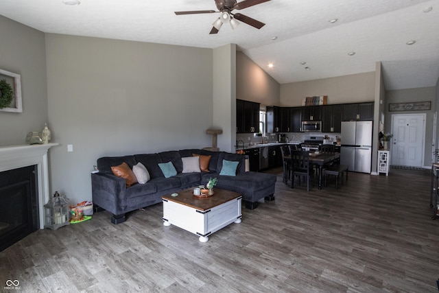 living room with dark wood-type flooring, ceiling fan, high vaulted ceiling, and a fireplace