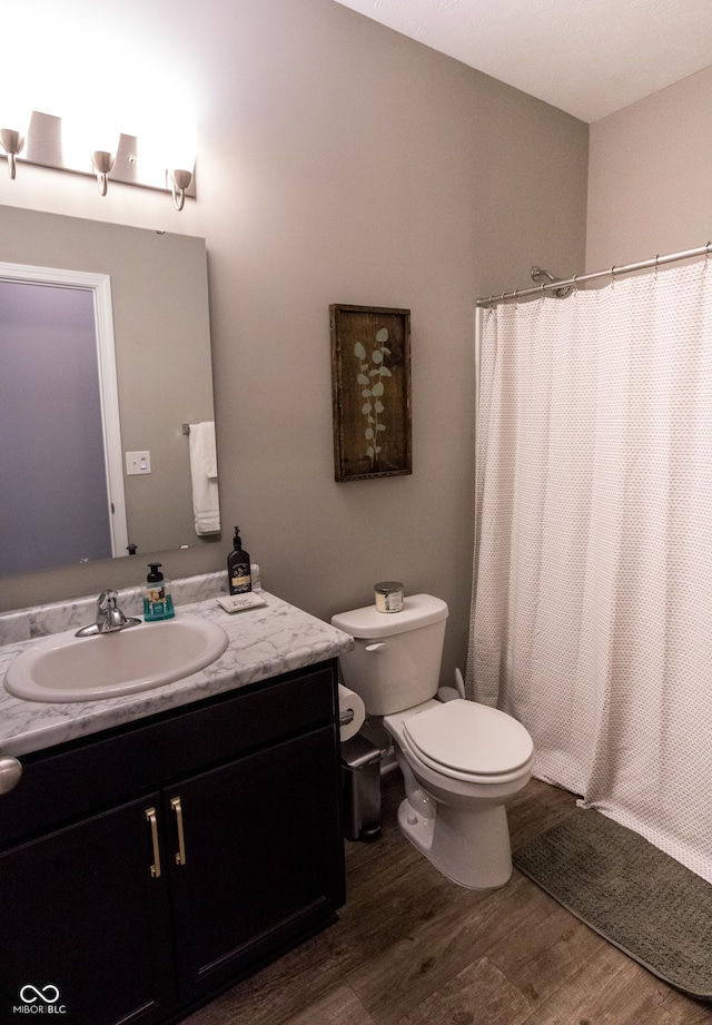 bathroom featuring toilet, curtained shower, wood finished floors, and vanity