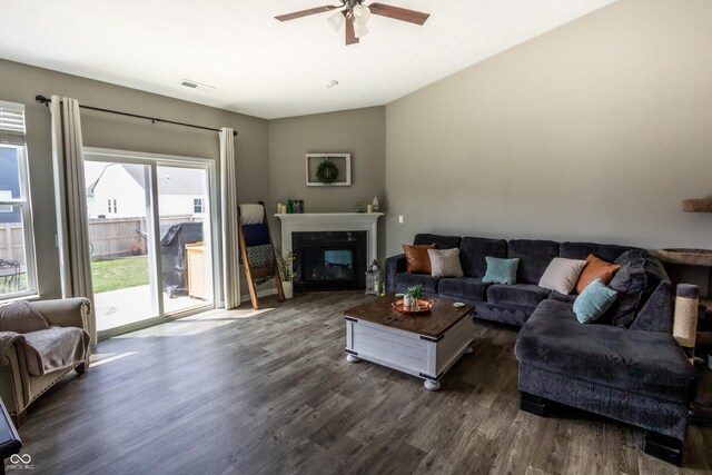 living room with visible vents, a glass covered fireplace, lofted ceiling, ceiling fan, and dark wood-type flooring