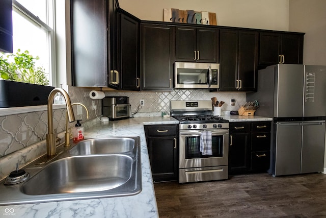 kitchen with dark wood-type flooring, tasteful backsplash, light stone counters, a sink, and stainless steel appliances