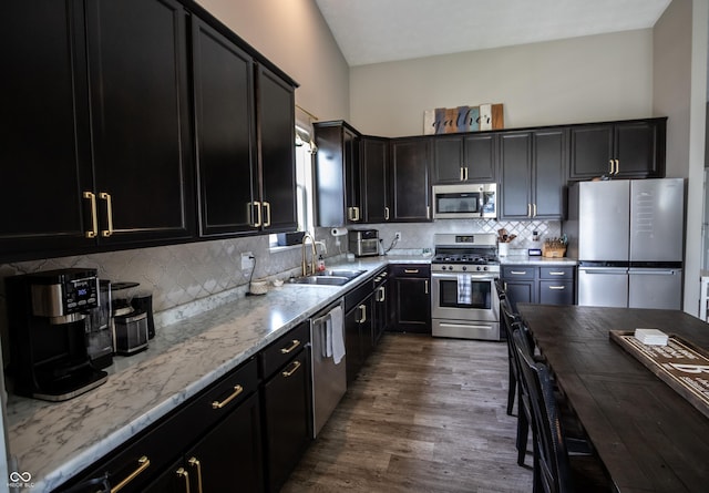 kitchen featuring light stone counters, a sink, dark cabinetry, stainless steel appliances, and dark wood-style floors
