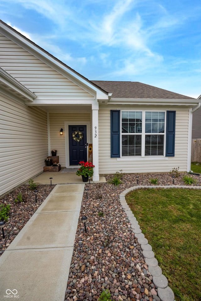 doorway to property with a shingled roof and a yard