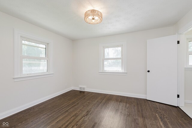 unfurnished room with baseboards, dark wood-style flooring, and visible vents