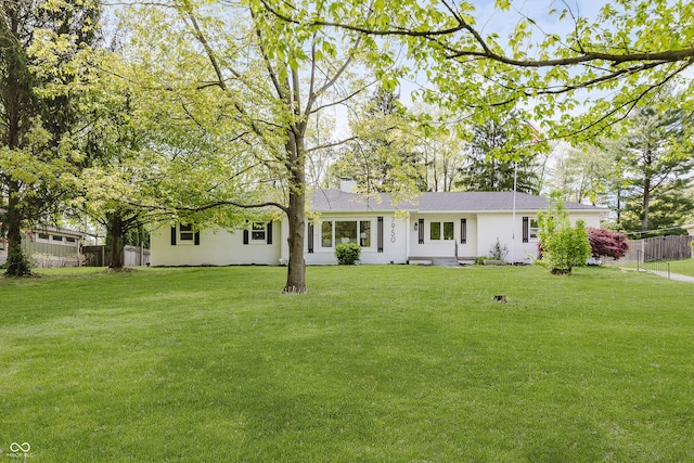 rear view of property featuring a lawn, fence, and stucco siding
