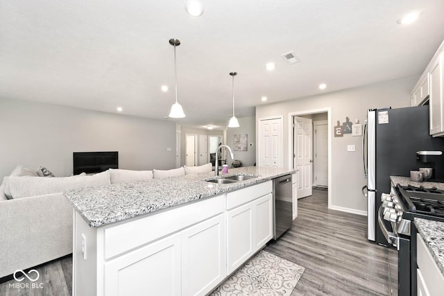 kitchen with appliances with stainless steel finishes, wood finished floors, a sink, white cabinets, and open floor plan