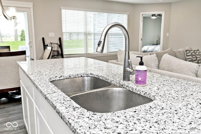 interior space featuring light stone counters, a sink, white cabinetry, open floor plan, and dark wood-type flooring