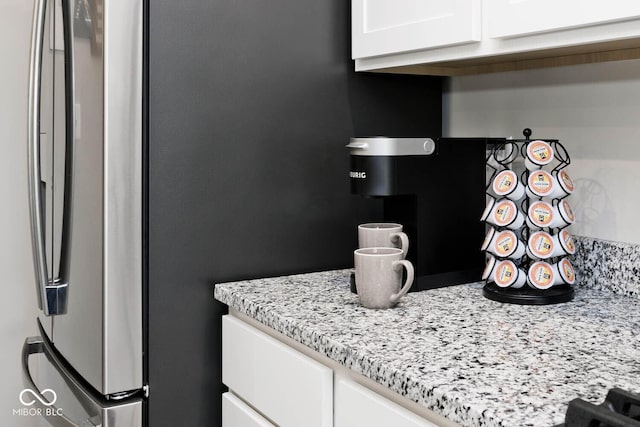 kitchen with light stone counters, freestanding refrigerator, and white cabinets