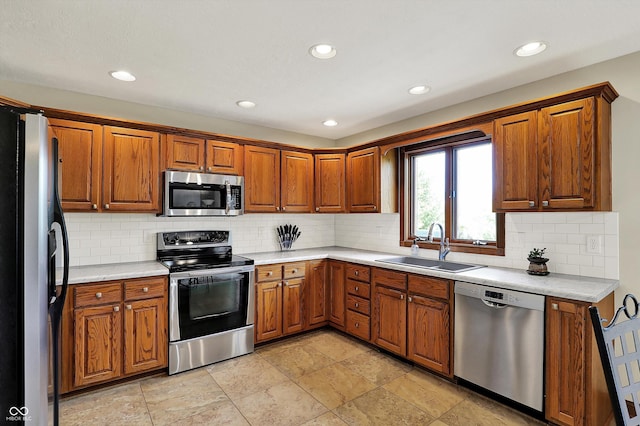kitchen featuring recessed lighting, brown cabinetry, a sink, light countertops, and appliances with stainless steel finishes
