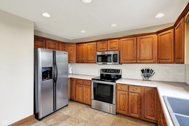 kitchen with a sink, backsplash, brown cabinets, light countertops, and appliances with stainless steel finishes