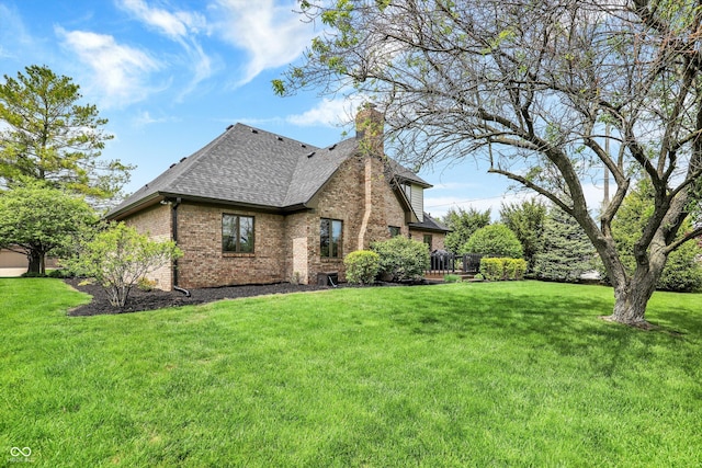 view of home's exterior featuring roof with shingles, a deck, brick siding, a yard, and a chimney