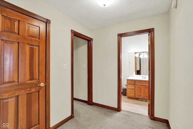 hall featuring light colored carpet, a textured ceiling, and baseboards
