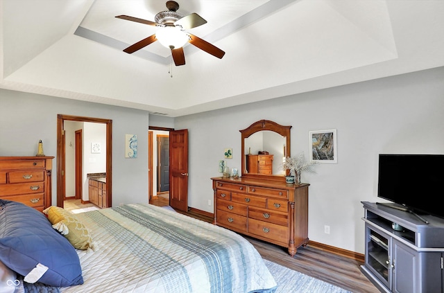 bedroom with ensuite bathroom, wood finished floors, a ceiling fan, a raised ceiling, and baseboards