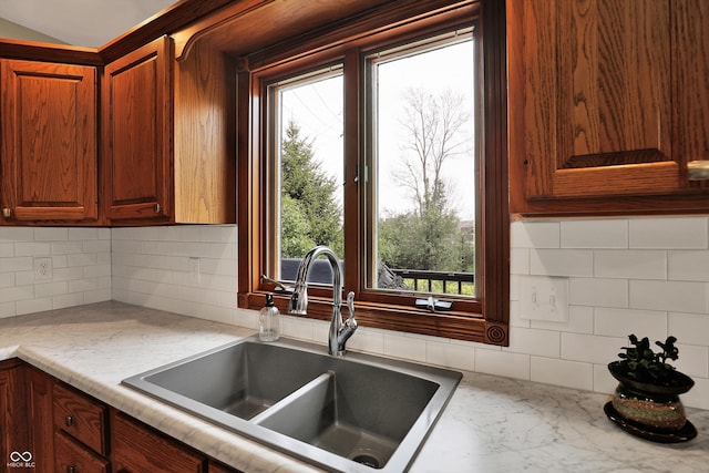 kitchen with a sink, light stone countertops, decorative backsplash, and plenty of natural light
