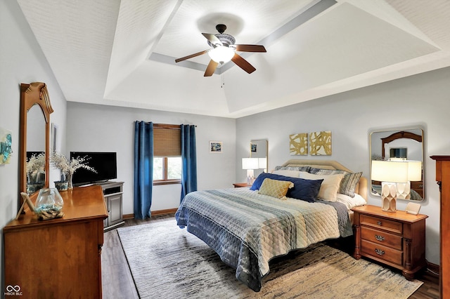 bedroom featuring ceiling fan, a raised ceiling, baseboards, and wood finished floors
