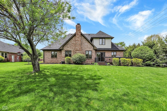 rear view of property with roof with shingles, a chimney, brick siding, and a lawn
