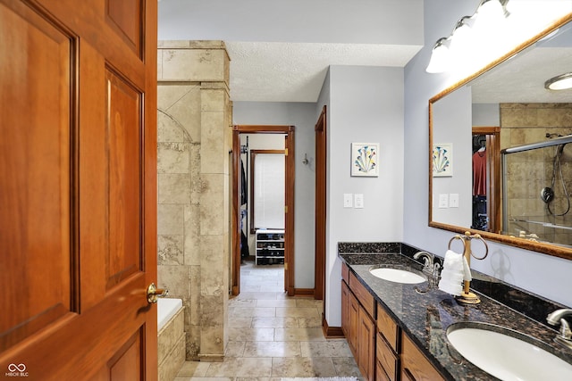 full bathroom featuring a tile shower, a textured ceiling, double vanity, and a sink