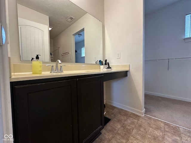bathroom featuring a textured ceiling, baseboards, vanity, and a shower