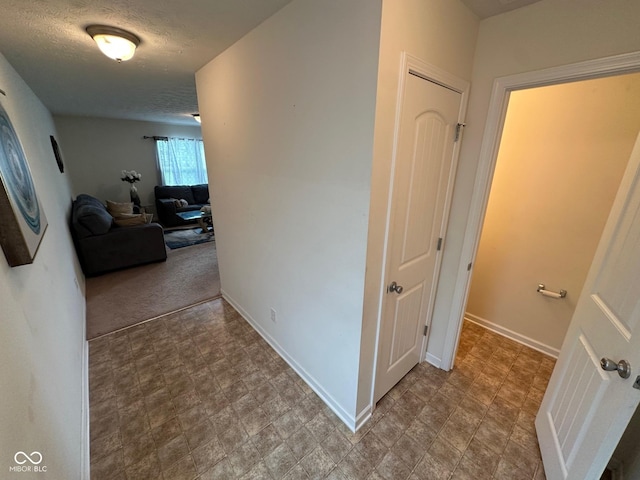 hall featuring baseboards, stone finish floor, and a textured ceiling