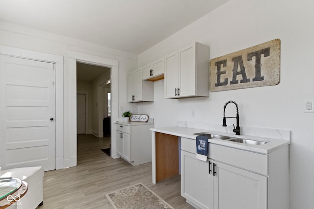 kitchen featuring a sink, light countertops, baseboards, light wood finished floors, and white cabinetry