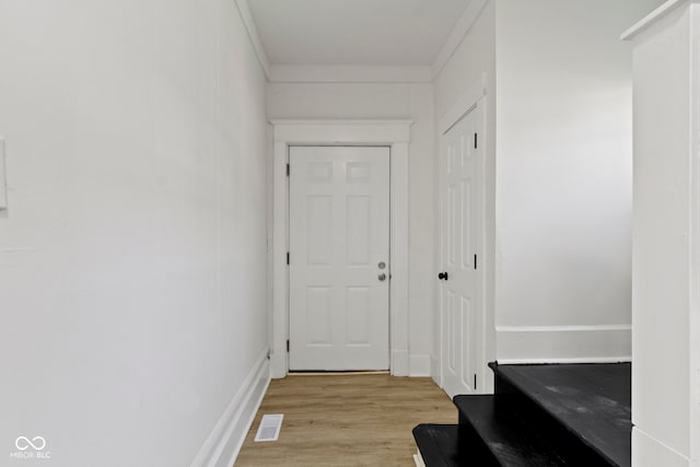 corridor featuring light wood-style floors, crown molding, and visible vents