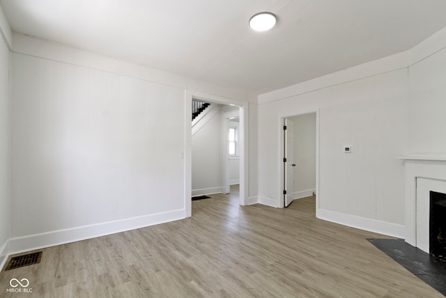 unfurnished living room with stairs, baseboards, a fireplace with flush hearth, wood finished floors, and visible vents