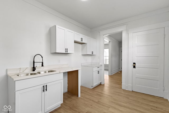 kitchen featuring white cabinetry, light stone counters, a sink, and light wood finished floors