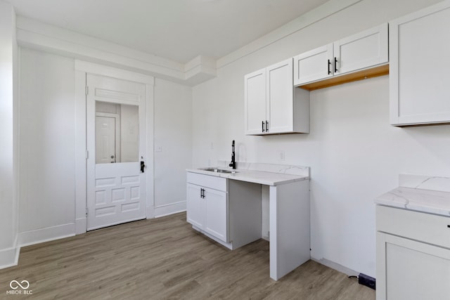 clothes washing area featuring baseboards, a sink, and light wood finished floors