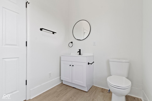 half bathroom with toilet, baseboards, wood finished floors, and vanity