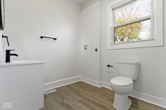 half bathroom featuring visible vents, wood finished floors, toilet, baseboards, and a sink
