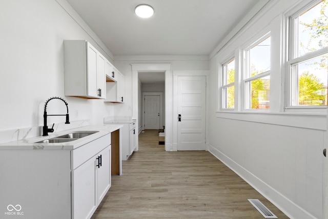 kitchen with visible vents, light stone countertops, white cabinets, a sink, and light wood-style flooring
