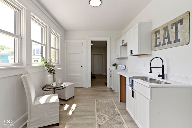 kitchen featuring white cabinets, a sink, light wood finished floors, and light countertops