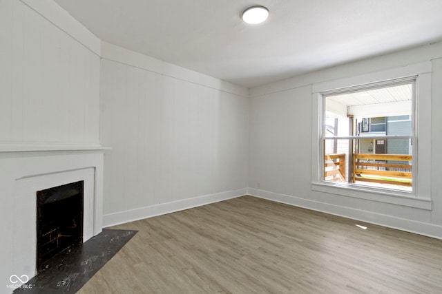 unfurnished living room featuring baseboards, a fireplace with flush hearth, and wood finished floors
