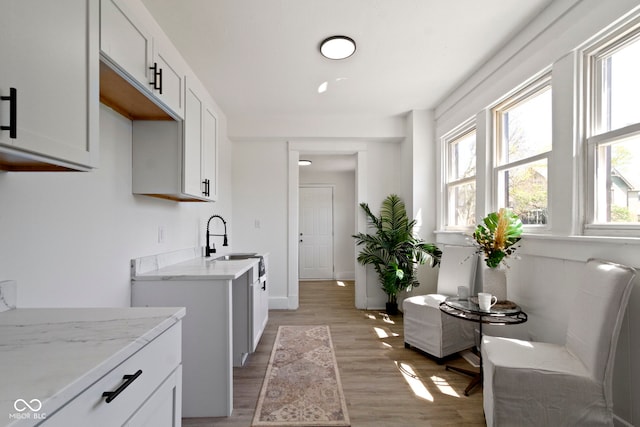 kitchen with a sink, white cabinets, light wood-style floors, and light stone countertops