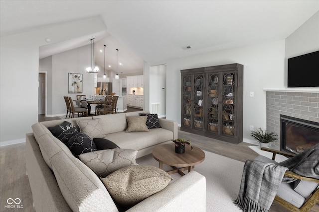 living area featuring wood finished floors, vaulted ceiling, a brick fireplace, a chandelier, and baseboards
