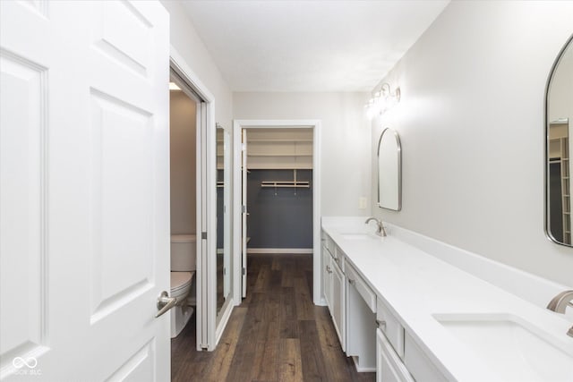 full bath featuring toilet, wood finished floors, a walk in closet, and double vanity