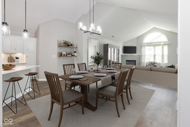 dining room with a fireplace, light wood finished floors, a chandelier, and high vaulted ceiling
