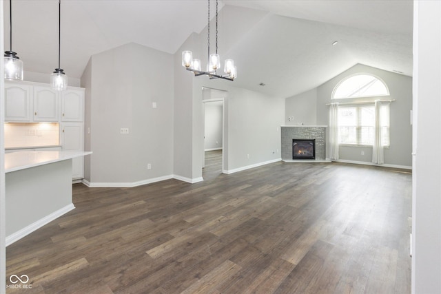 unfurnished living room featuring vaulted ceiling, a glass covered fireplace, dark wood-style floors, a chandelier, and baseboards