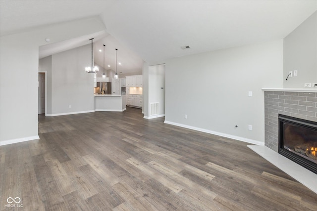 unfurnished living room with a fireplace, vaulted ceiling, a chandelier, dark wood-style floors, and baseboards