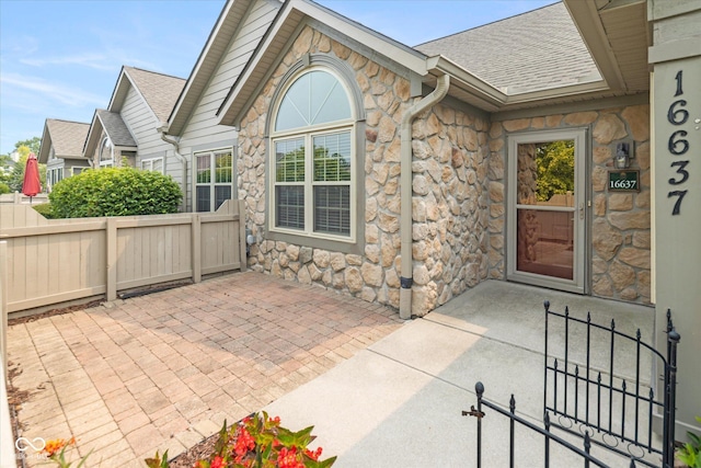 property entrance with stone siding, a patio, fence, and roof with shingles