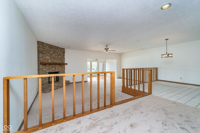 carpeted spare room featuring a ceiling fan, a stone fireplace, a textured ceiling, tile patterned floors, and baseboards