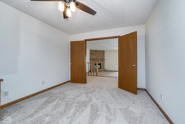 spare room featuring baseboards, a ceiling fan, carpet flooring, and a stone fireplace