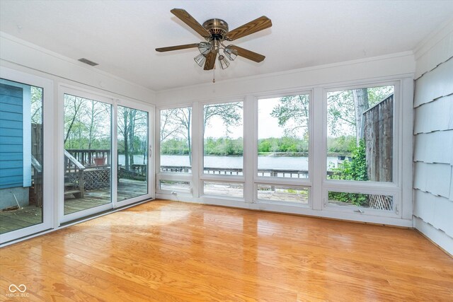 unfurnished sunroom featuring crown molding, a water view, wood finished floors, and visible vents
