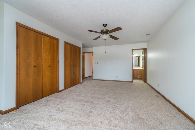 unfurnished bedroom featuring light colored carpet, baseboards, ensuite bath, and two closets