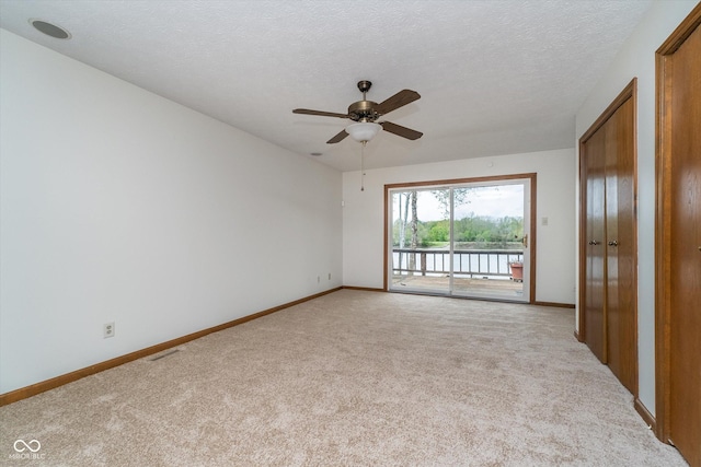 unfurnished room featuring light colored carpet, baseboards, ceiling fan, and a water view